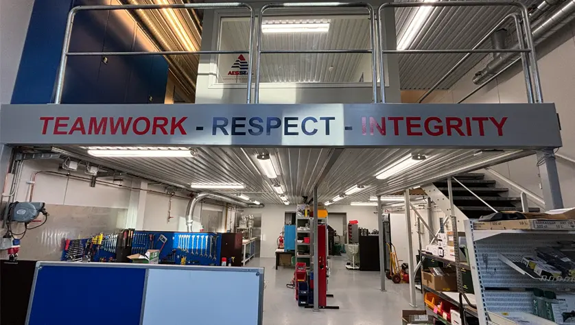 A clean assembly room with a mezzanine. The words 'teamwork, respect, integrity' are printed on the mezzanine.